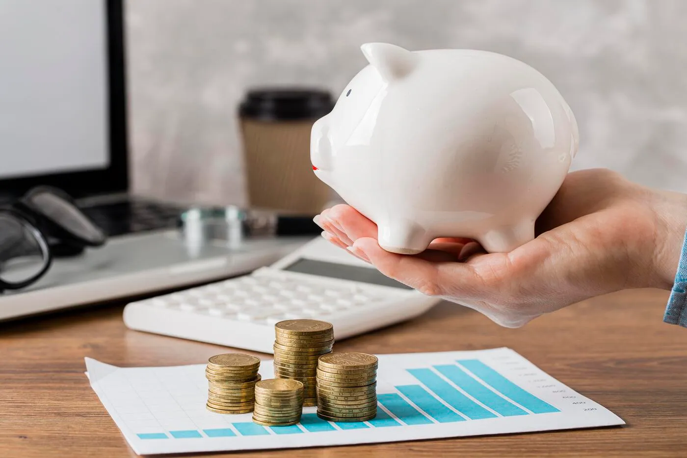 Foto de cofre em formato de porquinho sobre mesa com pilhas de moedas e planilha de crescimento, simbolizando controle financeiro e economia de custos administrativos