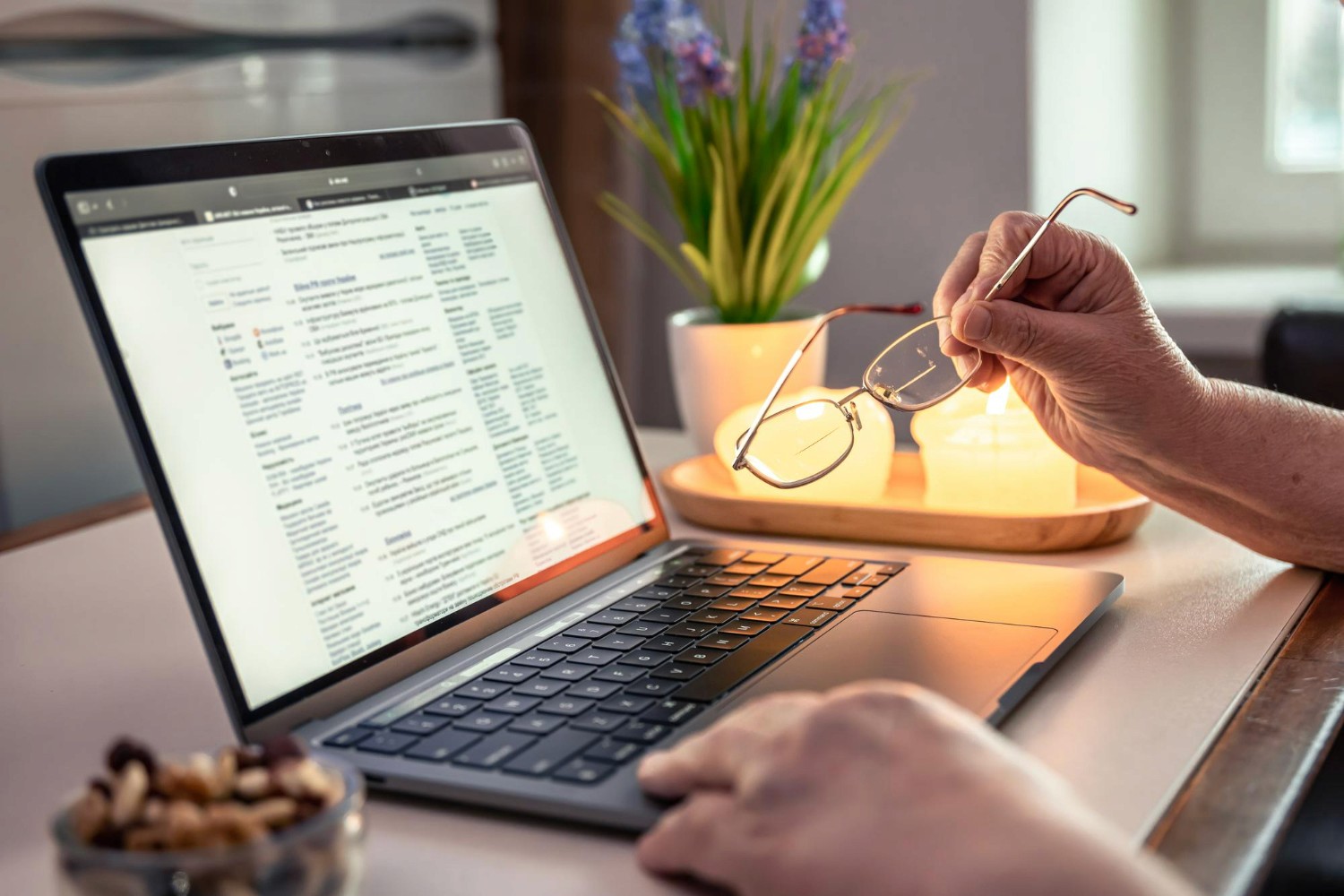 Pessoa consultando site em notebook, com óculos na mão em ambiente de trabalho