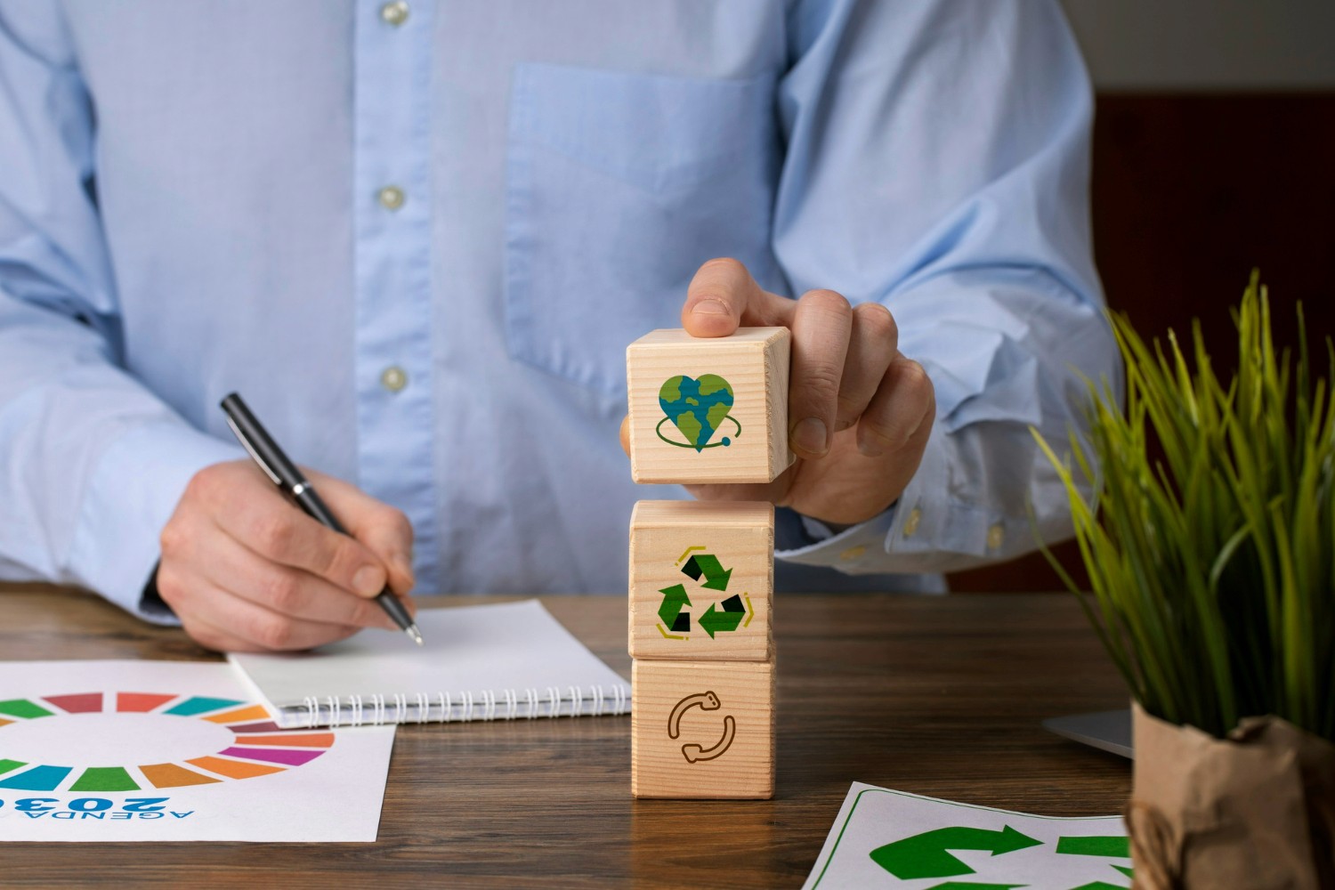 Pessoa empilhando blocos de madeira com ícones de sustentabilidade sobre mesa com Agenda 2030