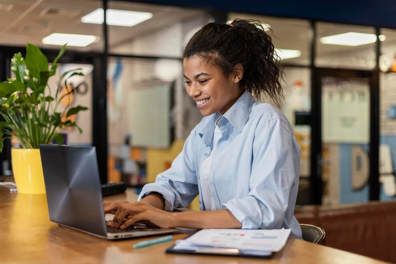 Mulher sorrindo enquanto trabalha em um notebook em ambiente corporativo, simbolizando processos digitais e autodeclaratórios na gestão pública.