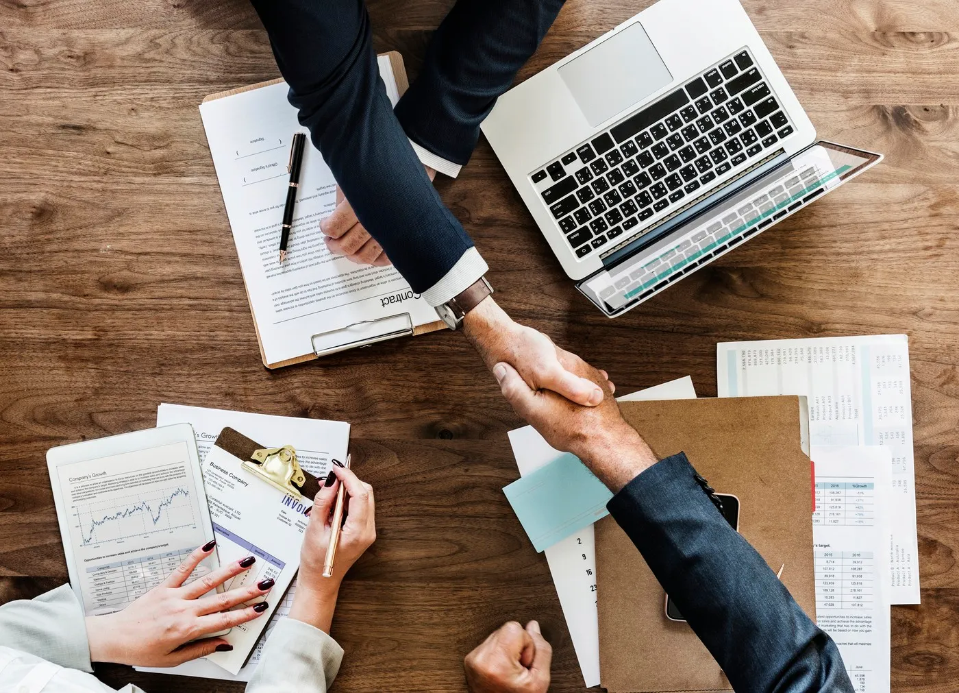 Reunião de negócios com documentos, contratos, gráficos e computador, simbolizando processos de licitação pública e tomada de decisão.